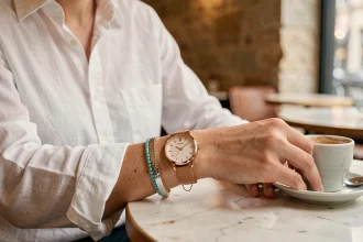 Femme portant une montre dorée et des bracelets empilés sur un poignet posé sur une table en marbre dans un café parisien